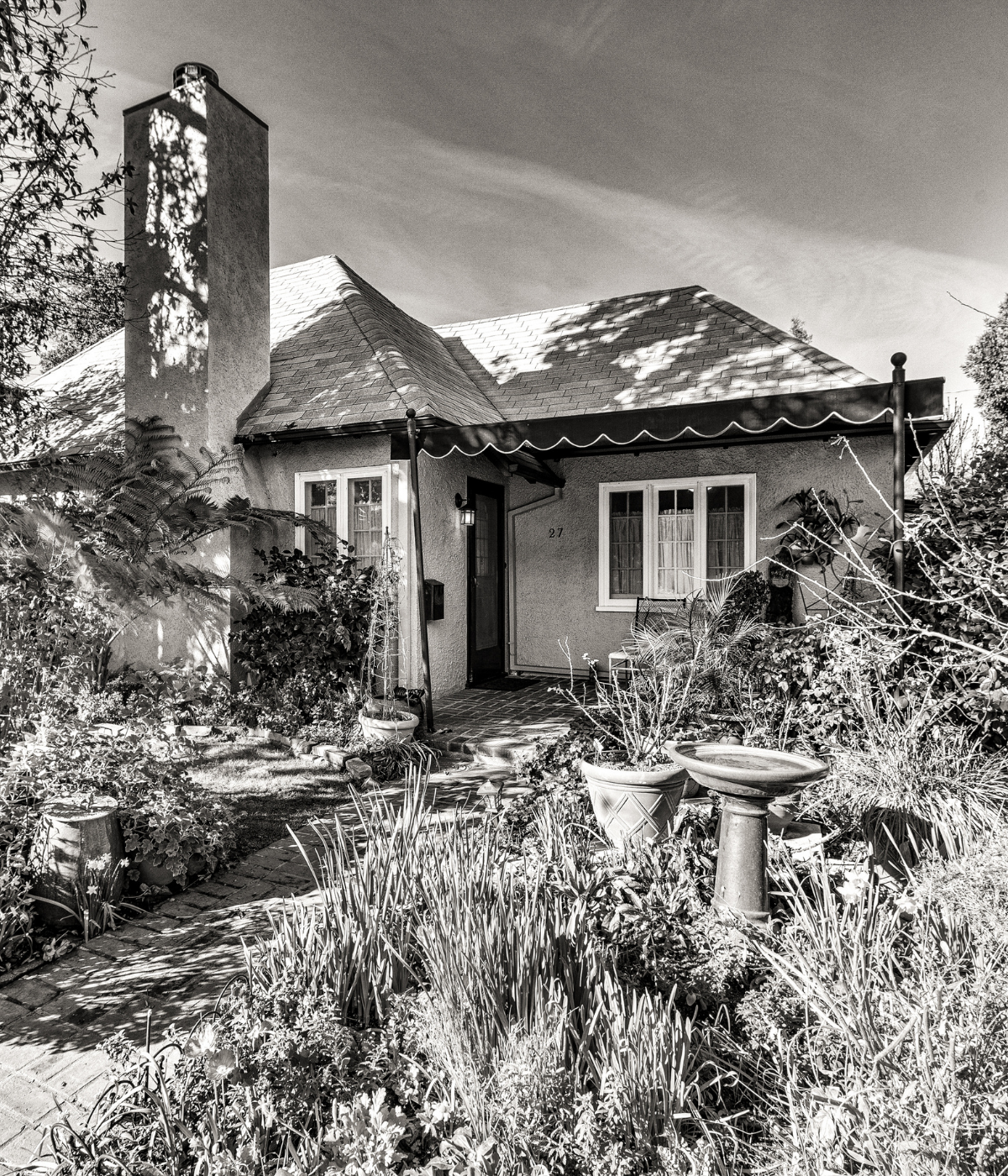 Black and white photograph of a classic California cottage with lush garden and brick pathway — celebrating 40 years of Wedgewood Homes